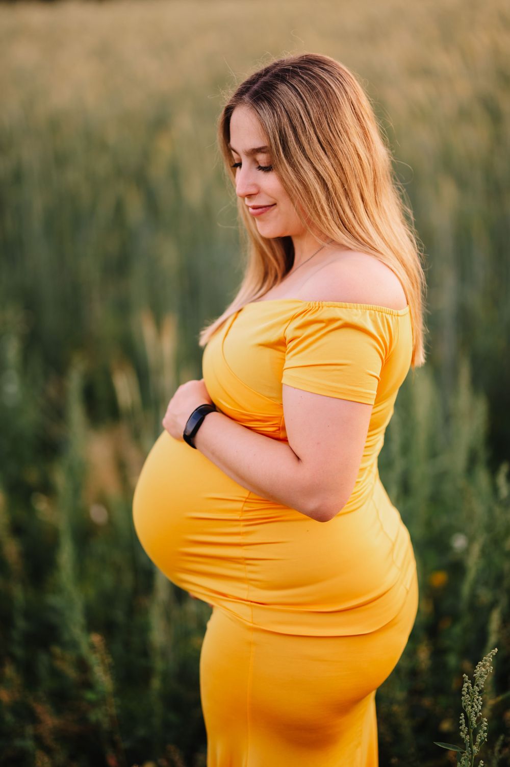 Maternity portrait in bright yellow dress against golden summer field at sunset.