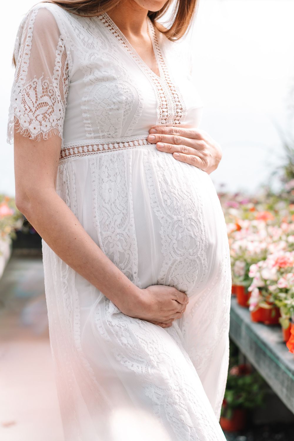 Close-up of pregnant belly in delicate white lace maternity dress with floral details.