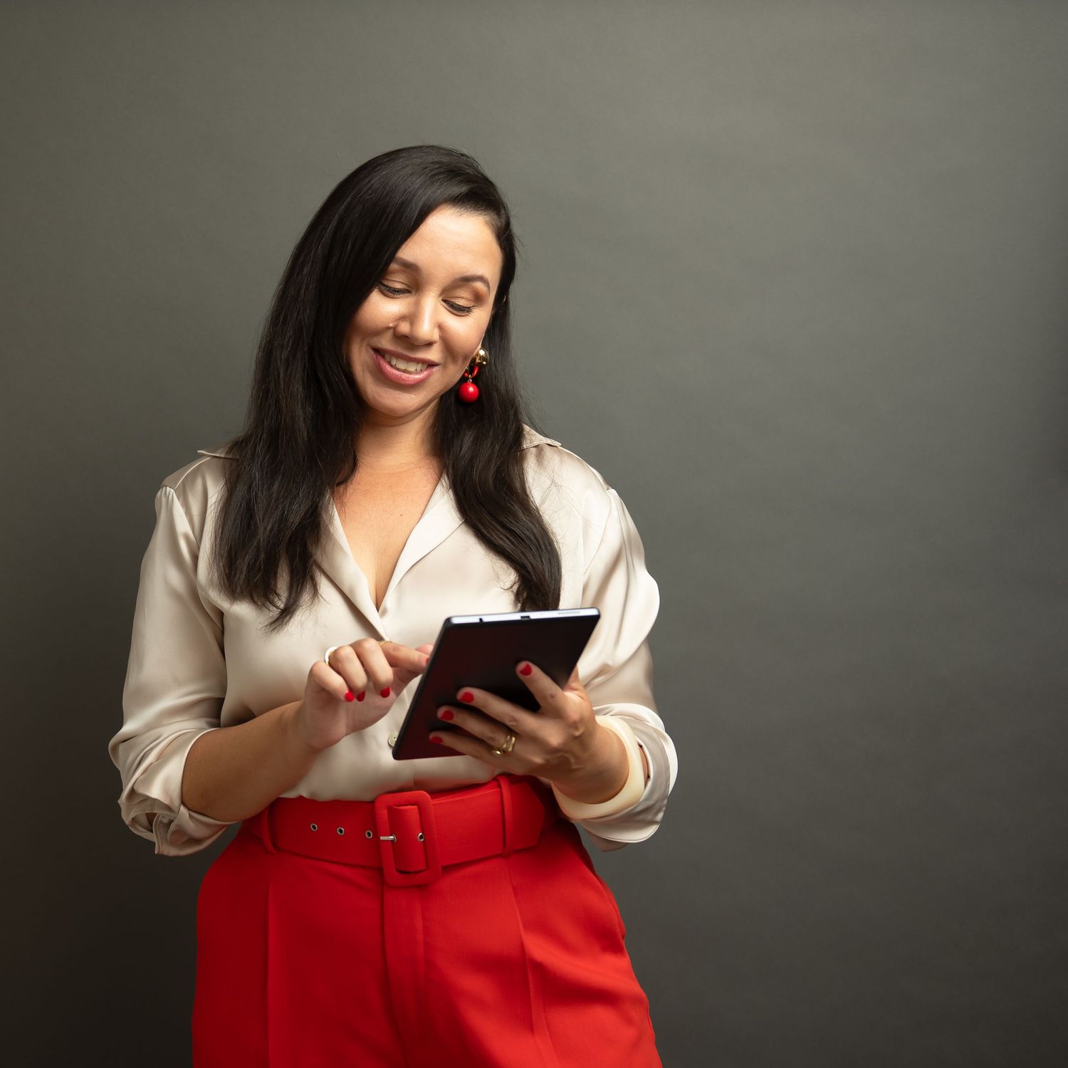 Business woman in white blouse and red skirt holding tablet while smiling.