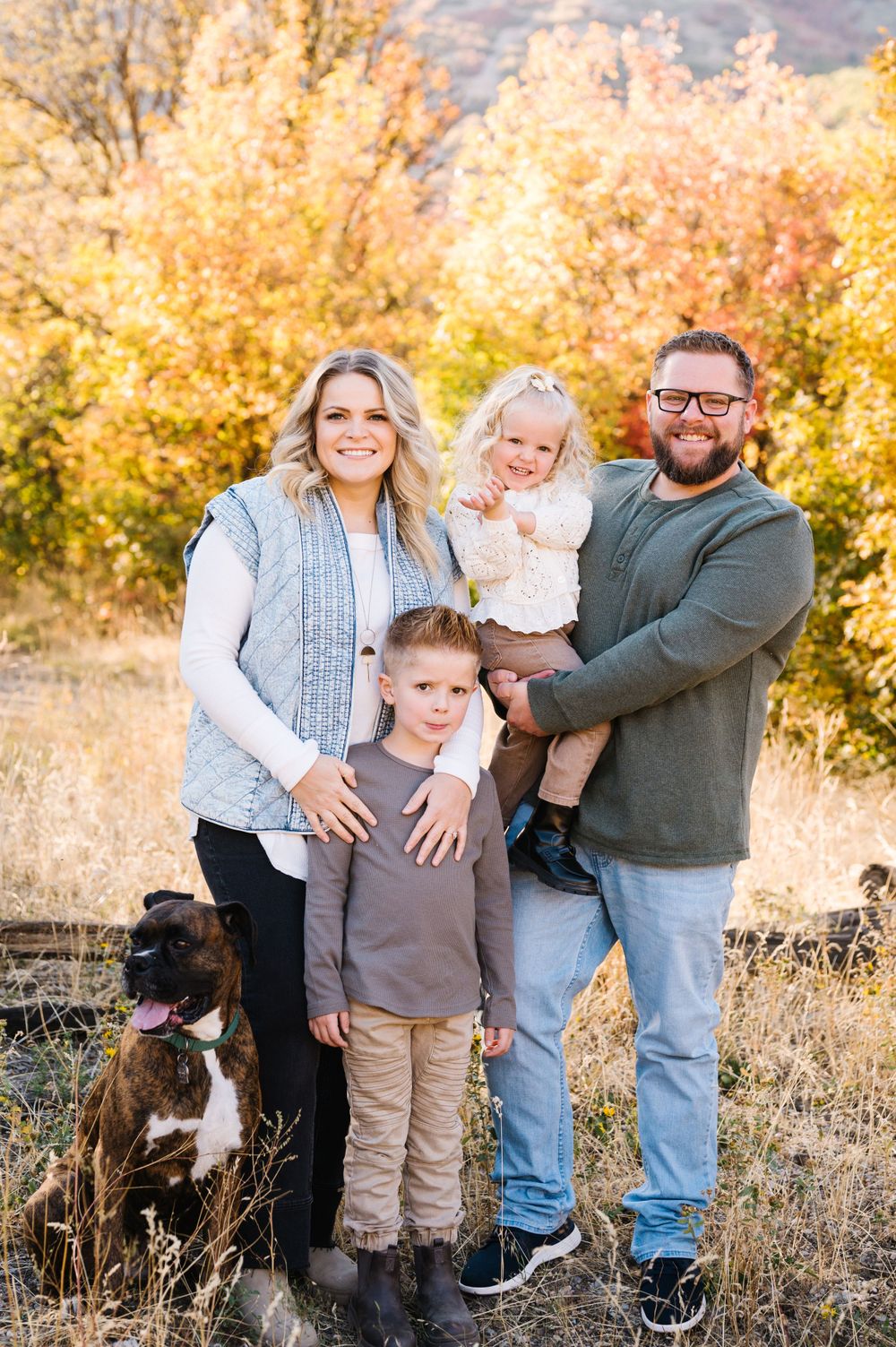 A family poses with their dog during autumn, surrounded by golden foliage.