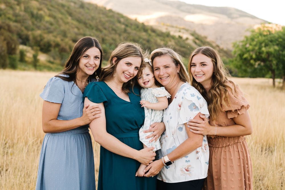Group in coordinated dresses poses together in golden mountain field at sunset.