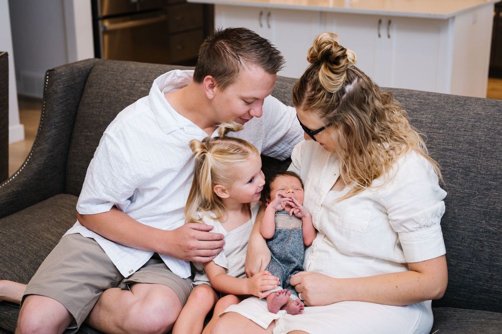 A family sitting together on a grey couch sharing a special moment with their newborn.
