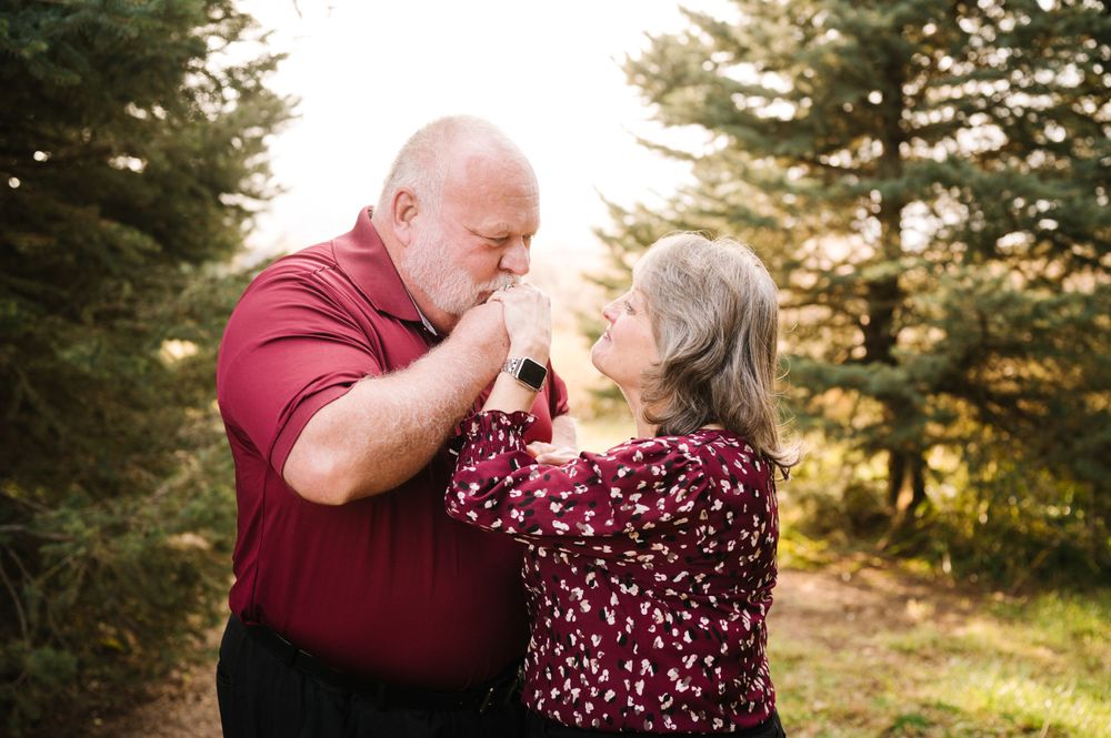 Older couple embracing outdoors with pine trees in background during sunset.