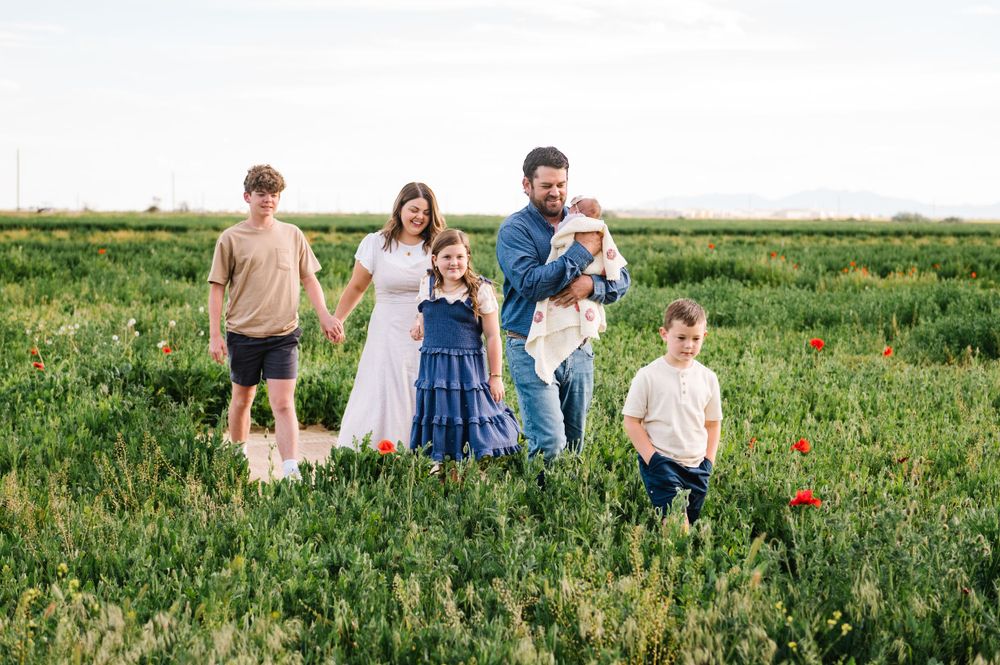 A family of six walking together through a wildflower meadow on a sunny day.