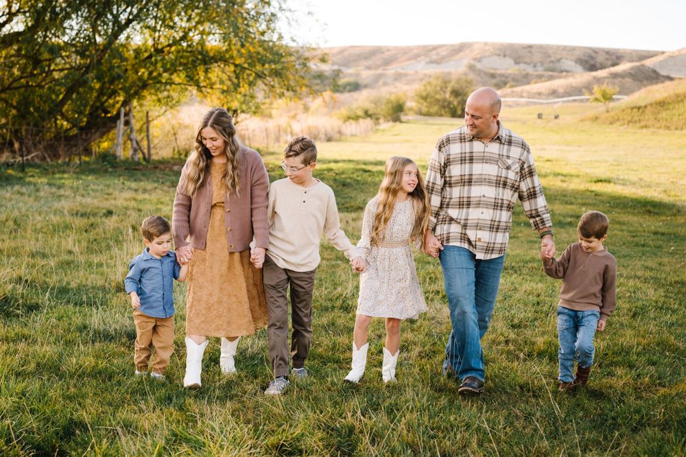 A family walks hand in hand through a grassy field during golden hour.