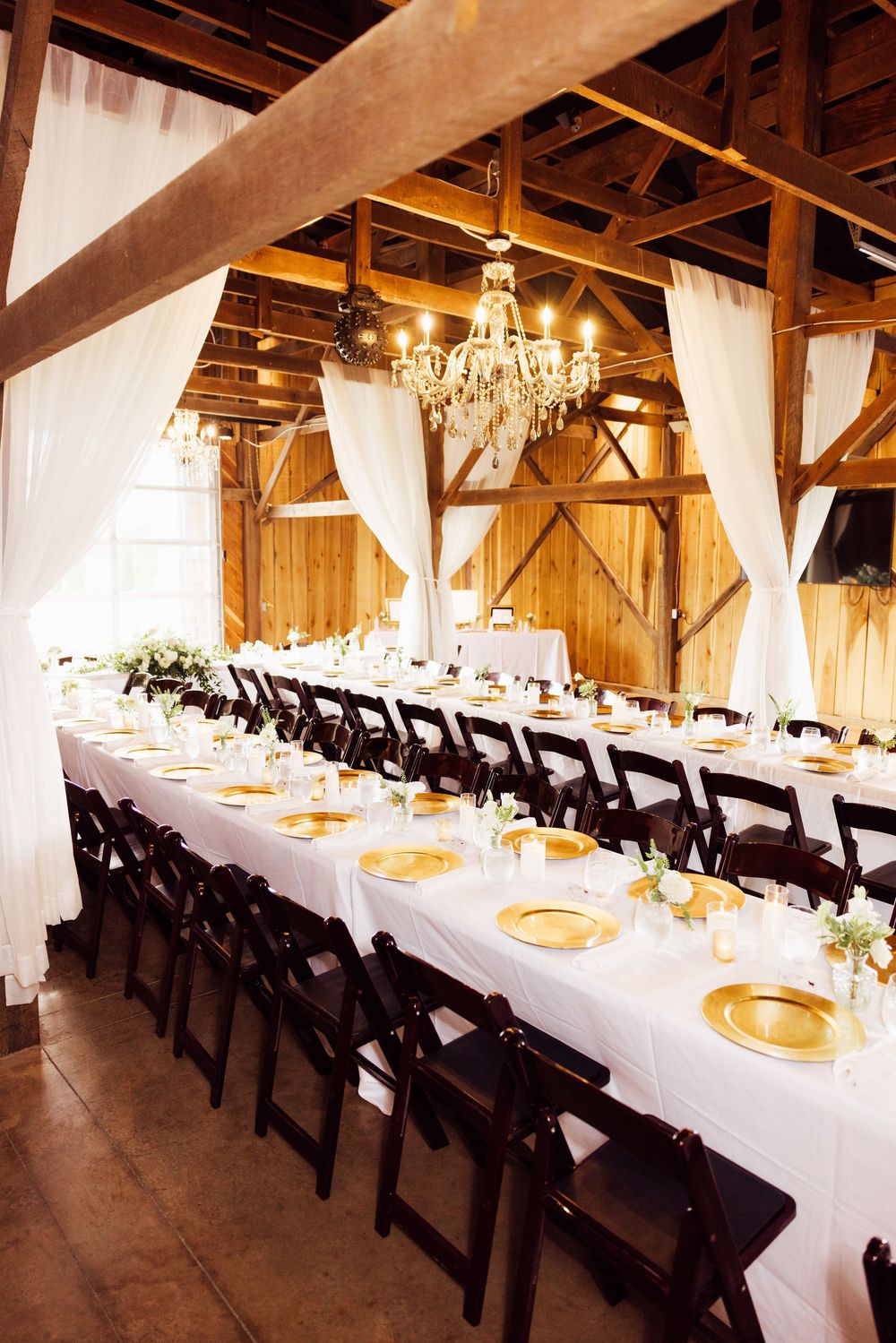 Event session with rustic barn wedding reception setup with white linens and black chairs.