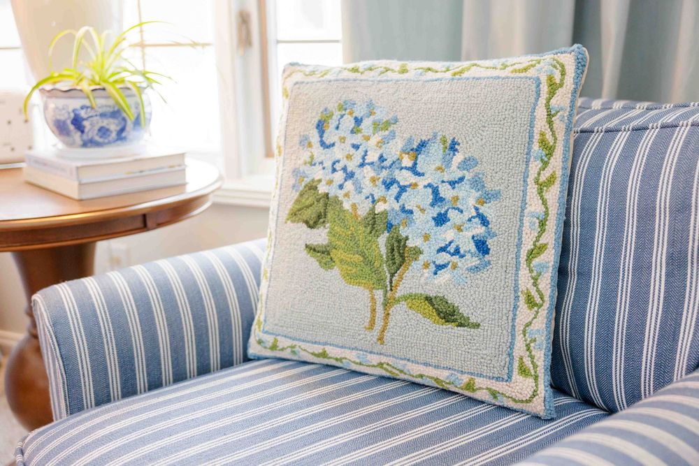 Boutique branding with hook pillow featuring blue hydrangea flowers on a striped couch.