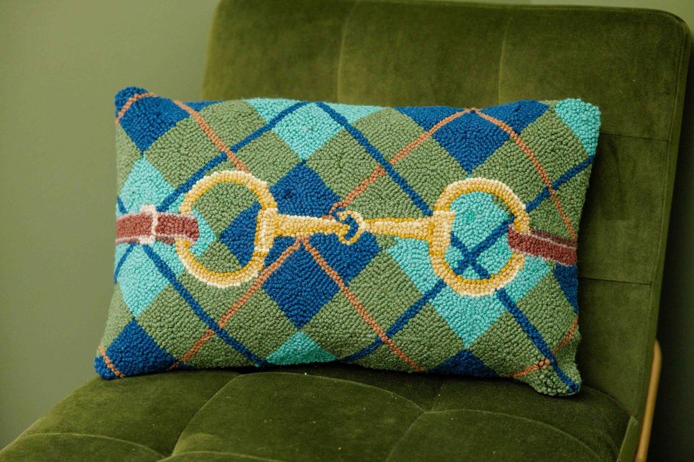Boutique branding with decorative pillow with blue and green argyle pattern and gold horse bit design.