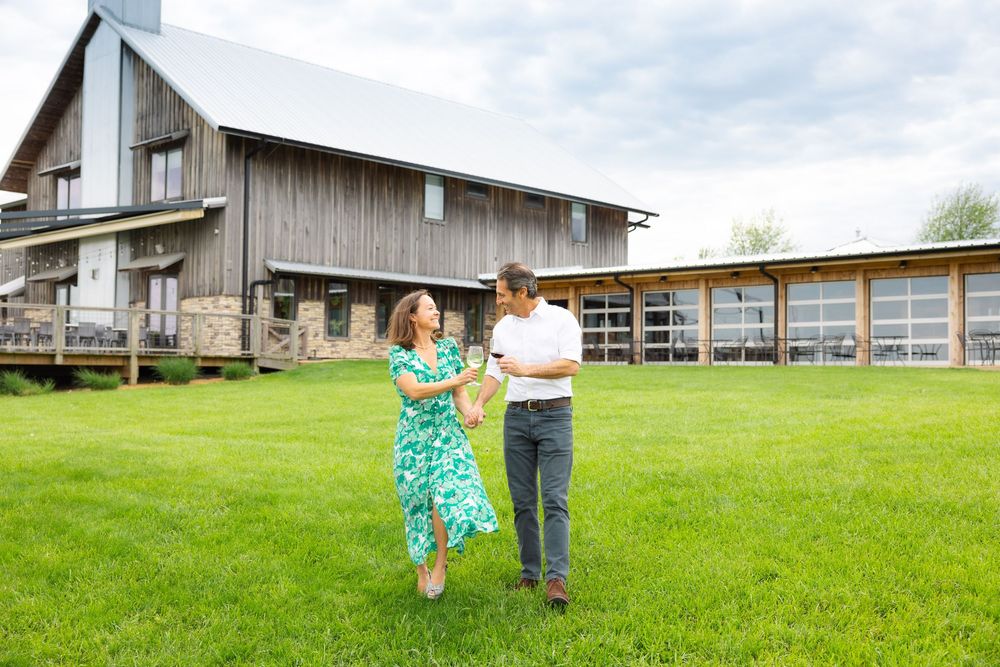Branding session with modern rustic buildings with large windows sit on a grassy hillside.