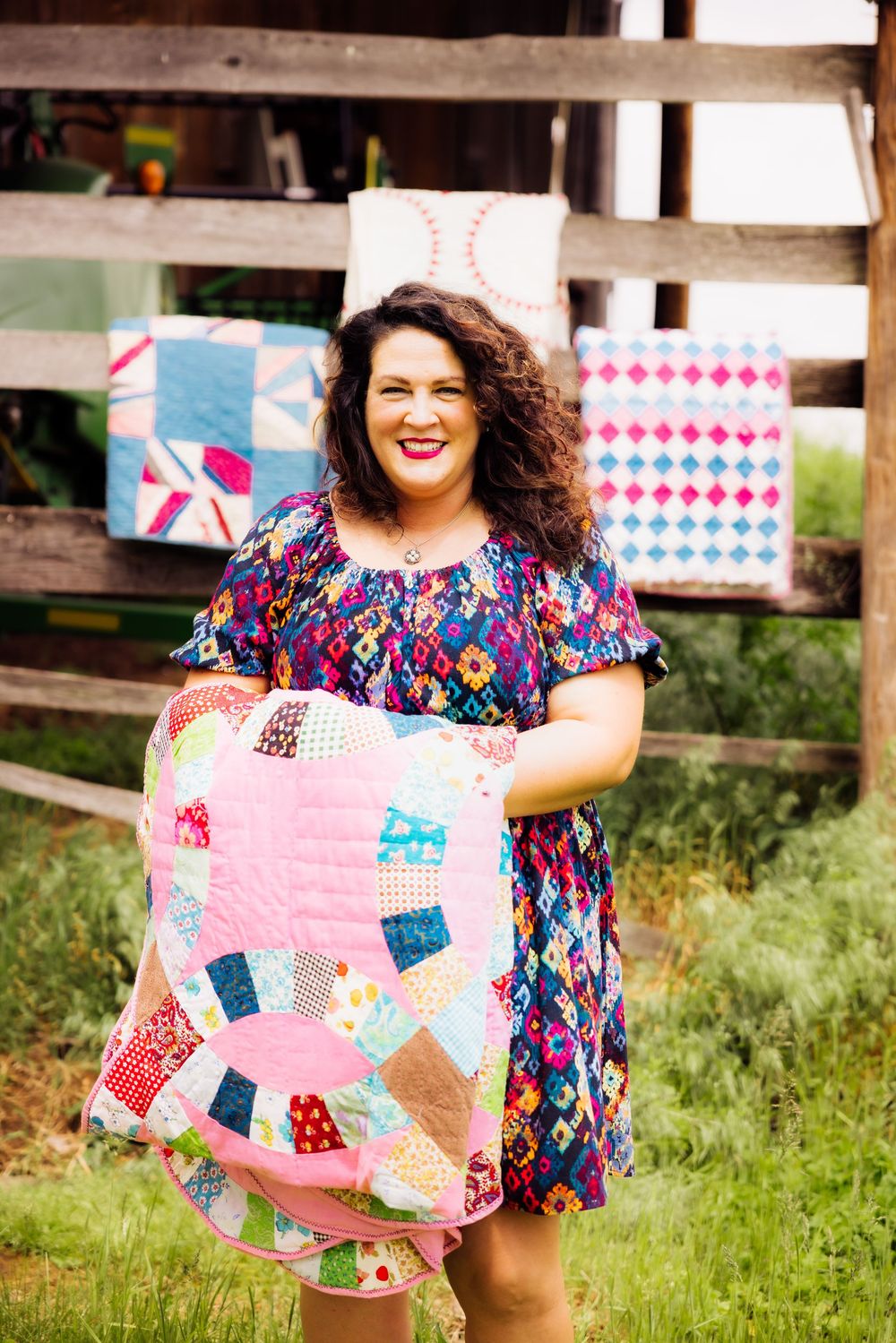 Branding session with colorful patchwork quilt displayed in front of rustic barn setting.