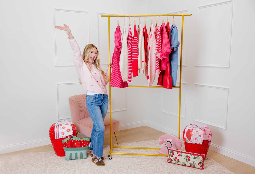 Boutique branding with pink and red clothing displayed on a gold clothing rack with decorative storage baskets.