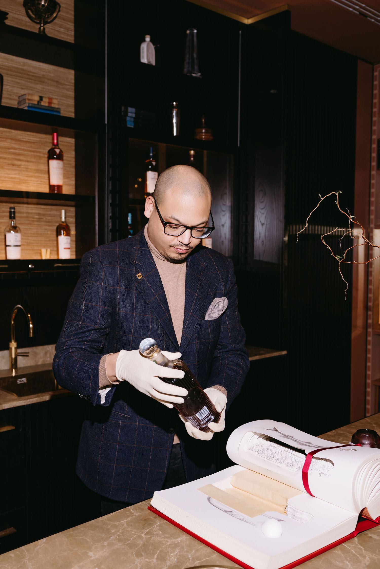 A person in a pinstripe suit examining bottles at a bar.
