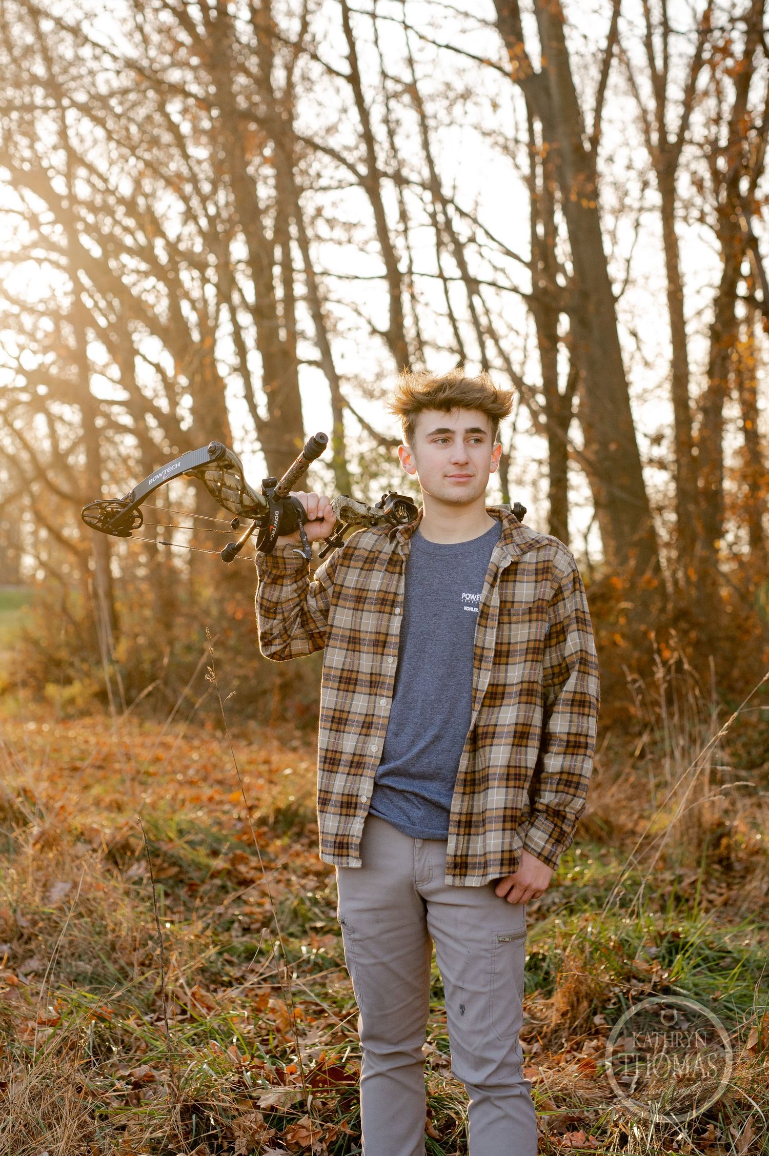 Outdoor portrait of bow hunter in plaid shirt standing among fall foliage.