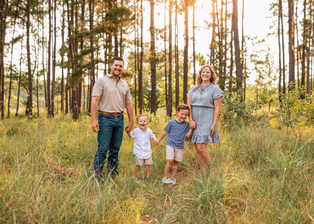 Family walking together through a sunlit pine forest during golden hour.