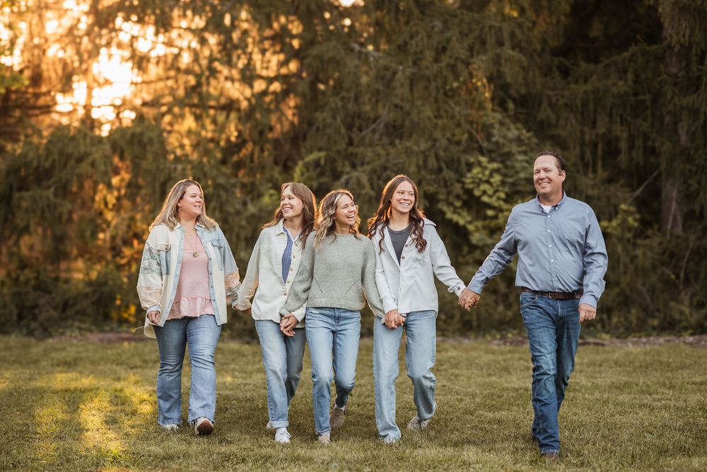 A family of 5 walking hand to hand laughing and playing in the golden light of the sunset.
