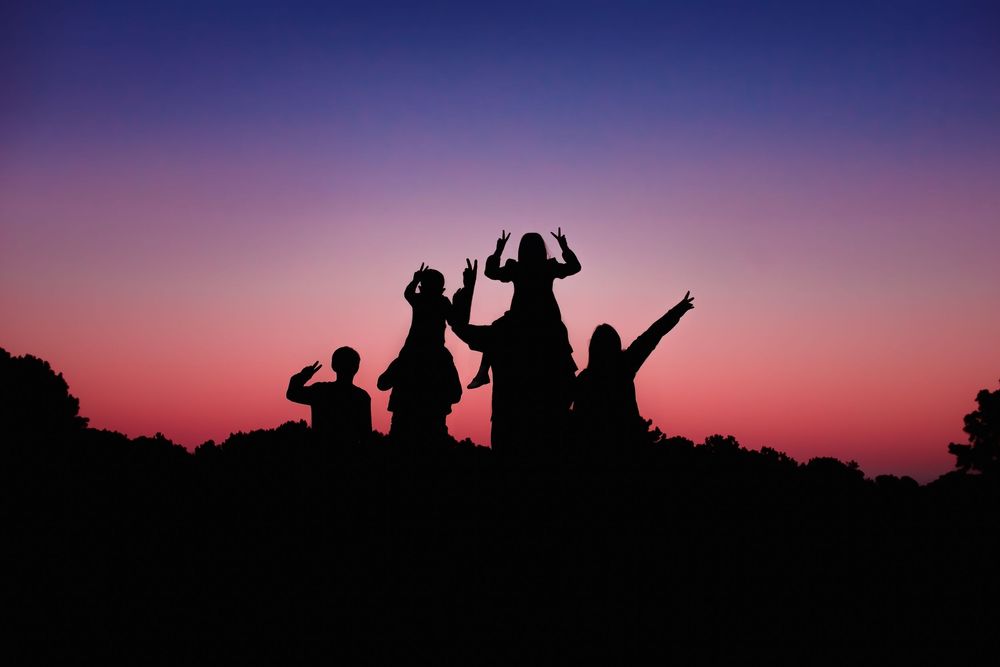 Silhouettes of people dancing and celebrating against a vibrant purple and pink sunset sky.