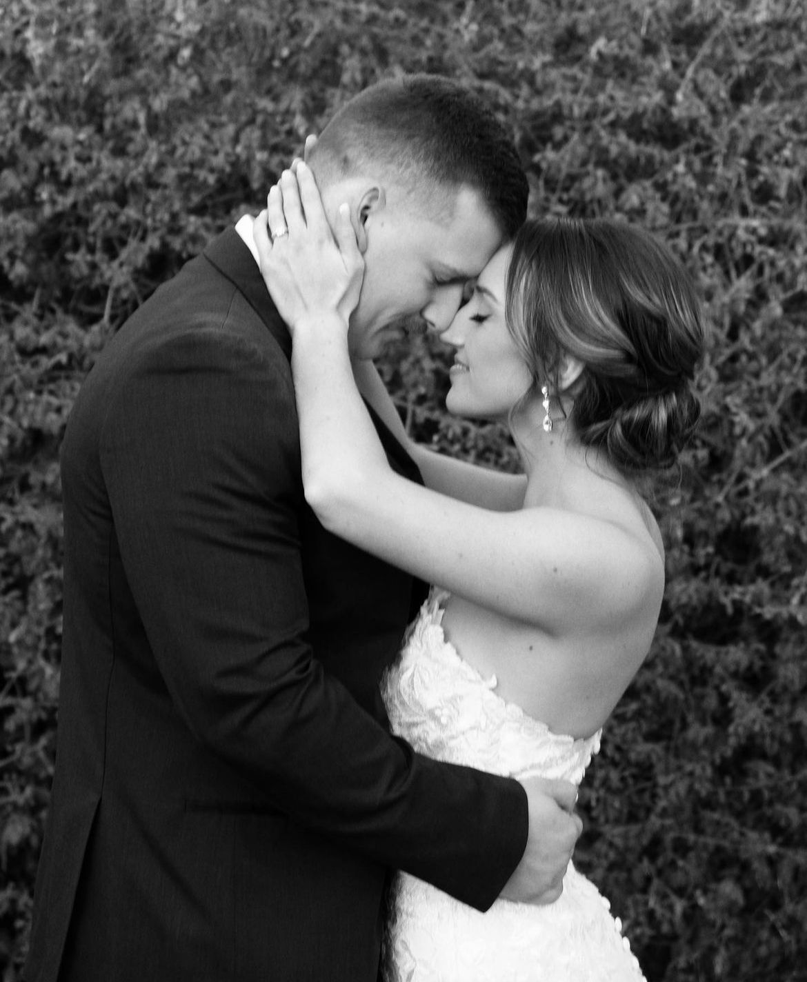 A tender black and white wedding portrait capturing an intimate moment between newlyweds against a garden backdrop.