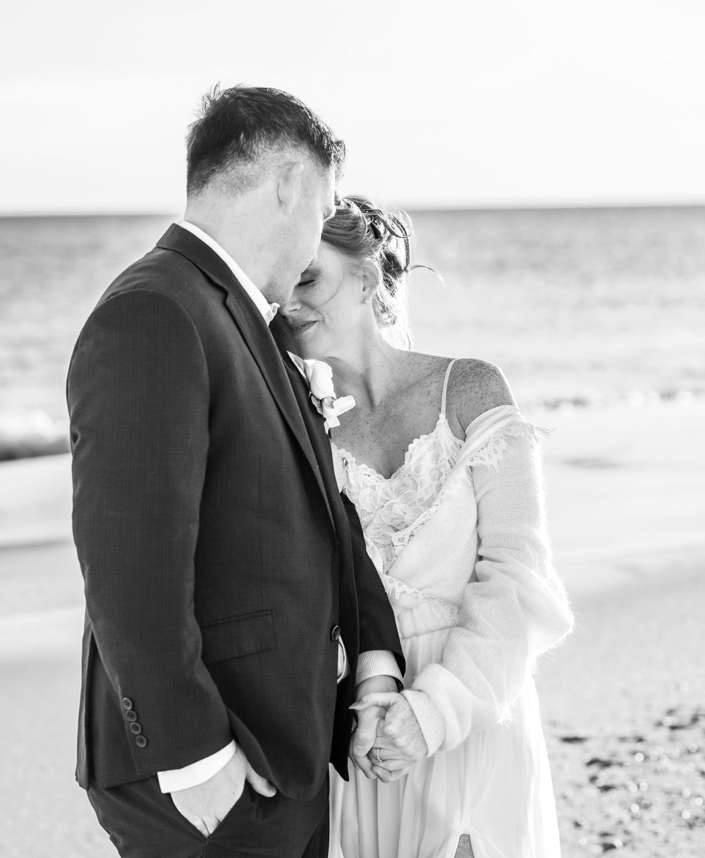 An intimate black and white beach wedding portrait of newlyweds standing close together at the ocean shore.