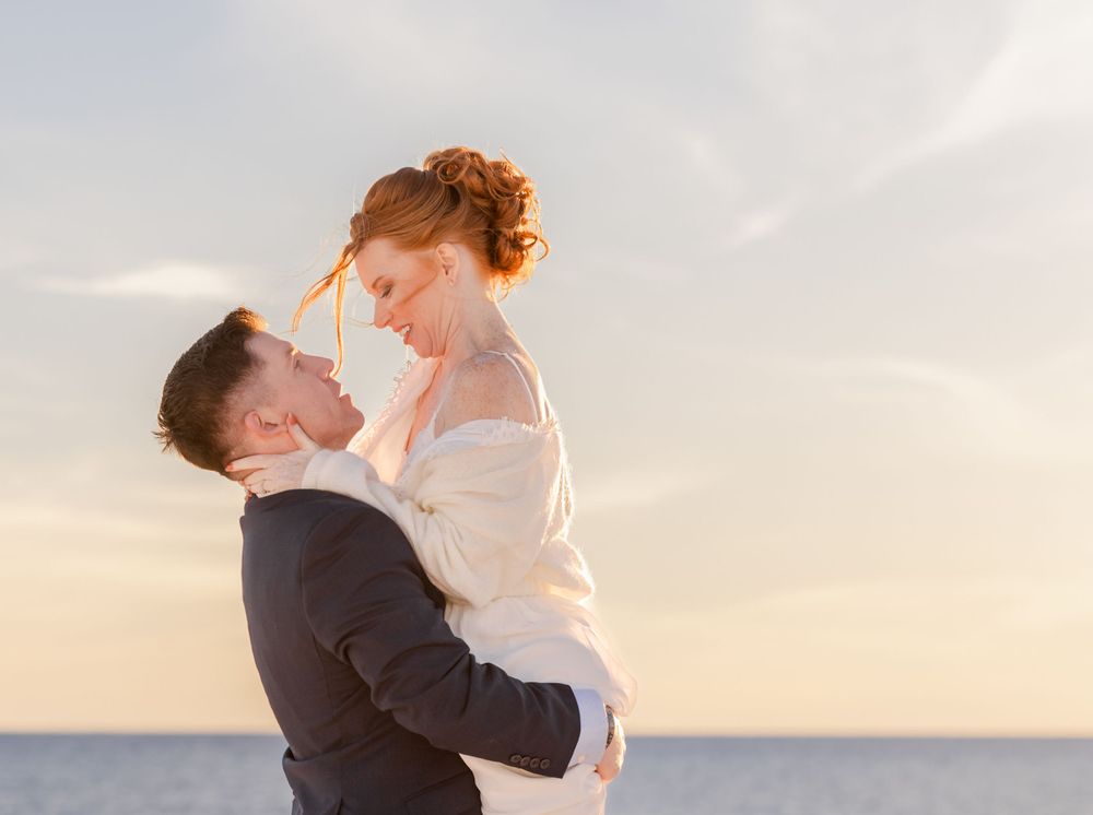 Romantic couple embracing at sunset by the ocean with soft golden light in the background.