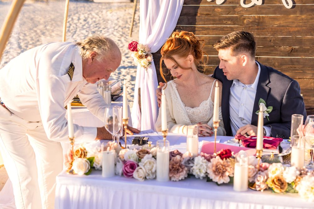 People sitting at an elegantly decorated wedding table with lush floral arrangements and candles at outdoor reception.