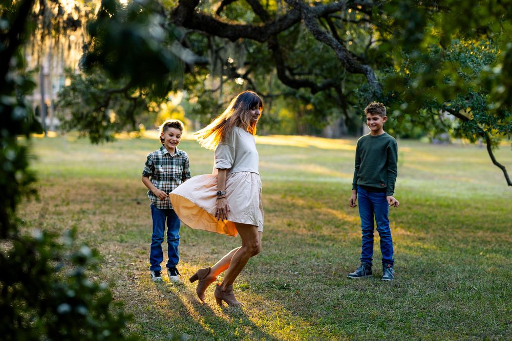 Family plays together in a park during golden hour under mossy oak trees at sunset.
