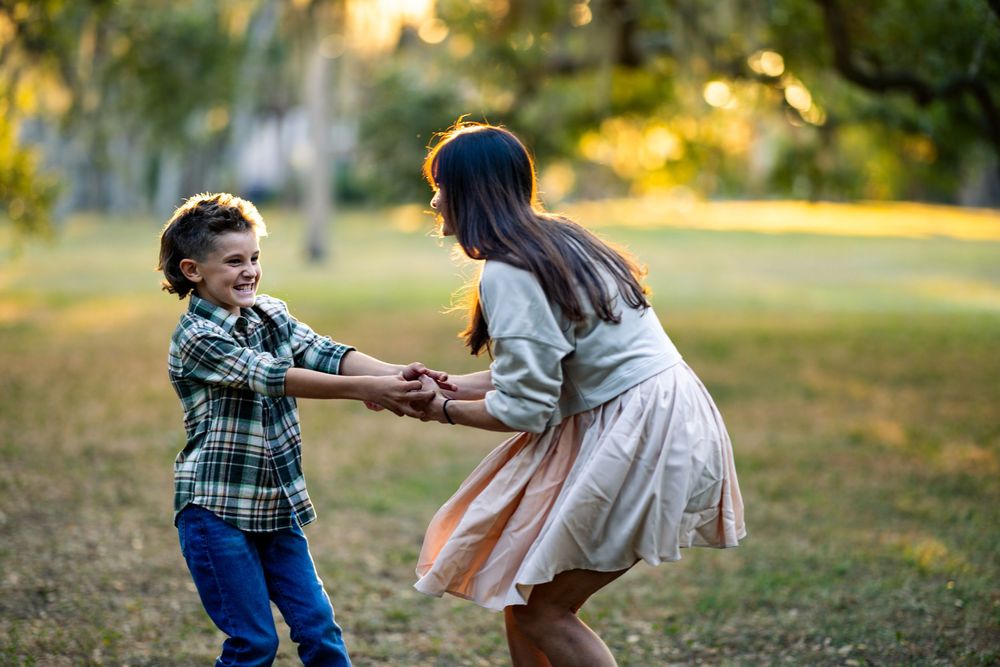 Two people playfully dance together in a sunlit park during golden hour.