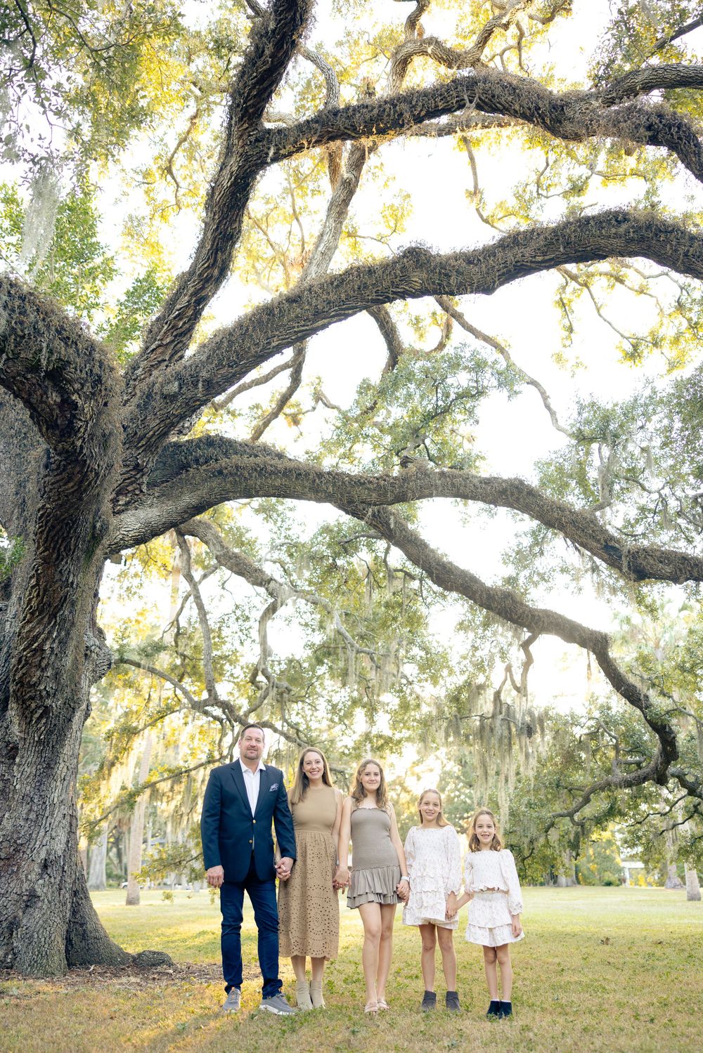 A group stands together under a majestic oak tree with hanging Spanish moss in a scenic outdoor setting.