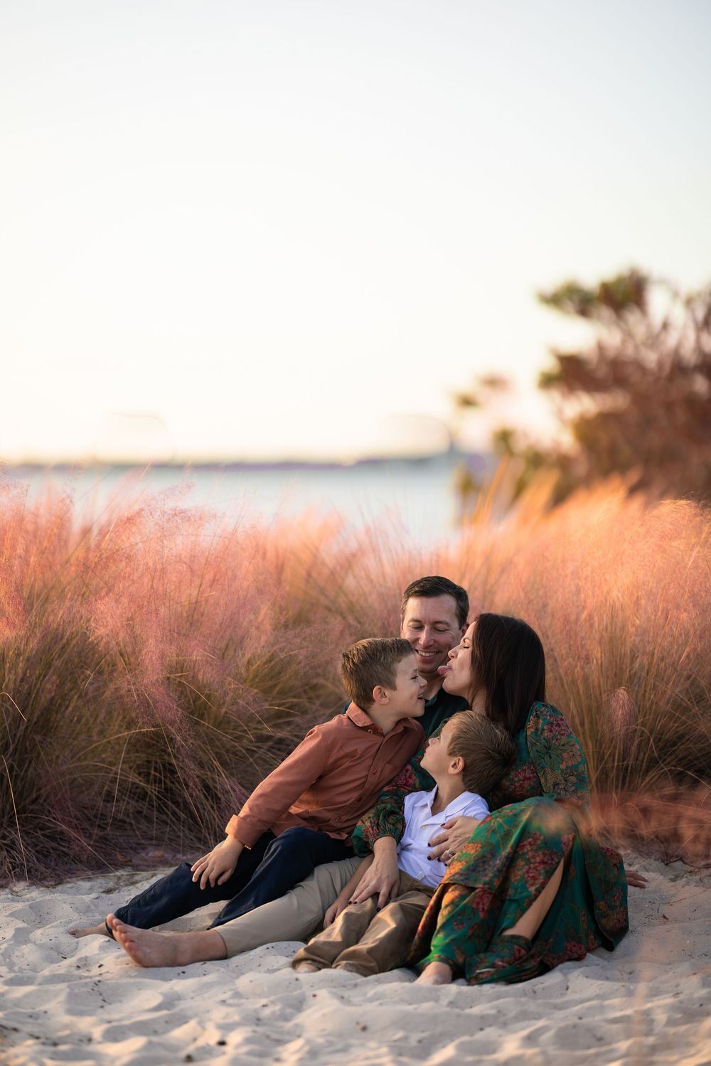 Family enjoying sunset together on sandy beach with tall grass in warm golden light.