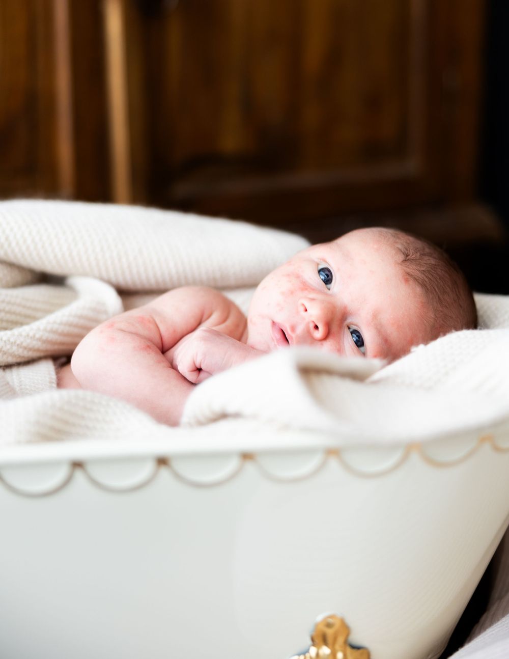 Baby lying in soft white bedding in a vintage bath tub cozy and bright with blue eyes.