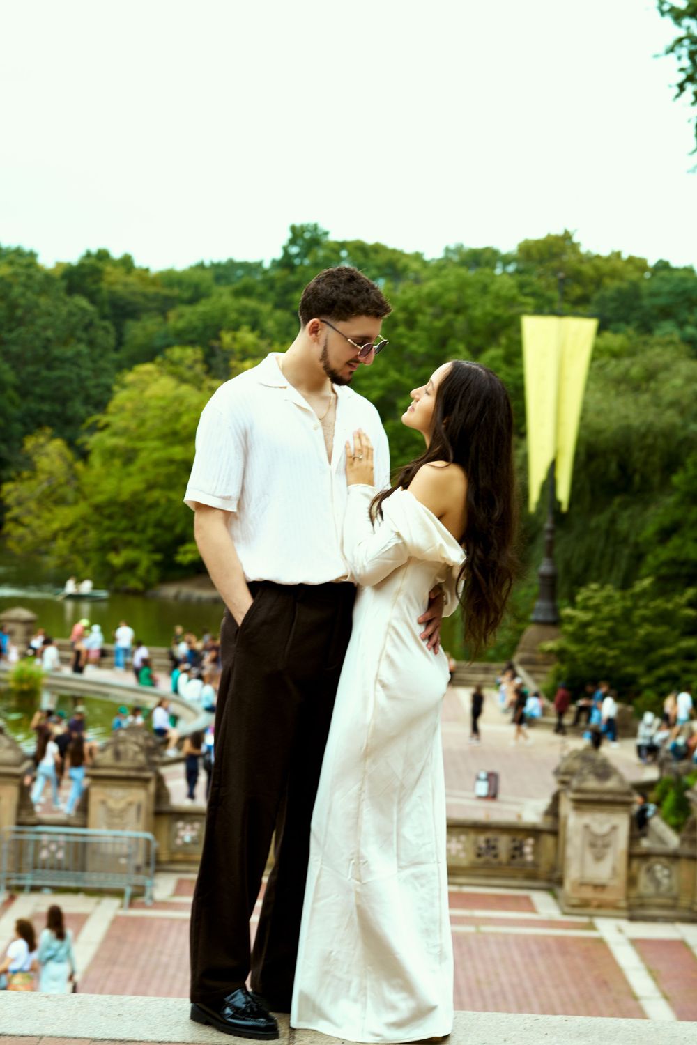 A couple in contrasting black and white outfits embrace at a crowded outdoor location.
