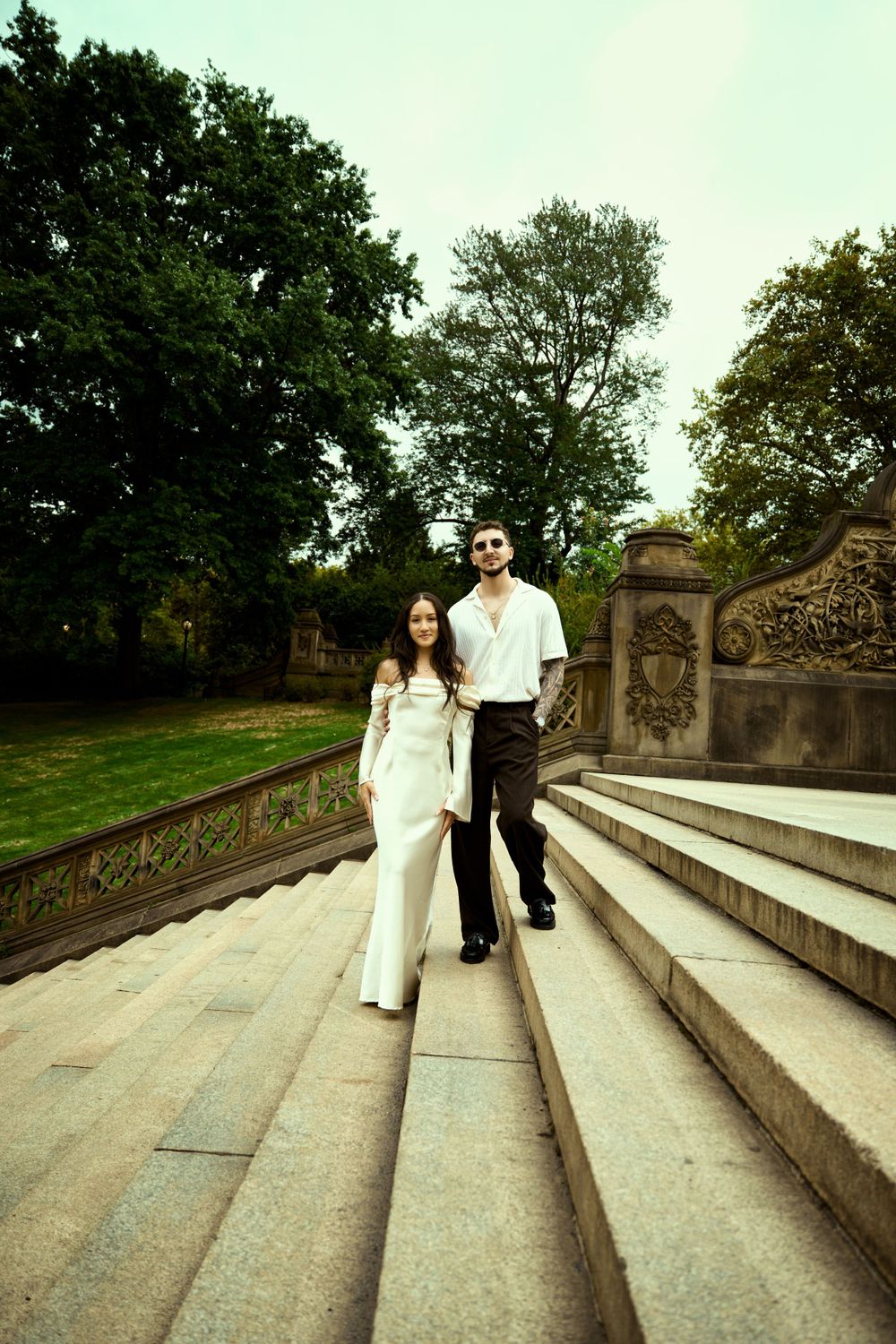 Couple walking up stone steps in formal white and black outfits at an outdoor garden setting.
