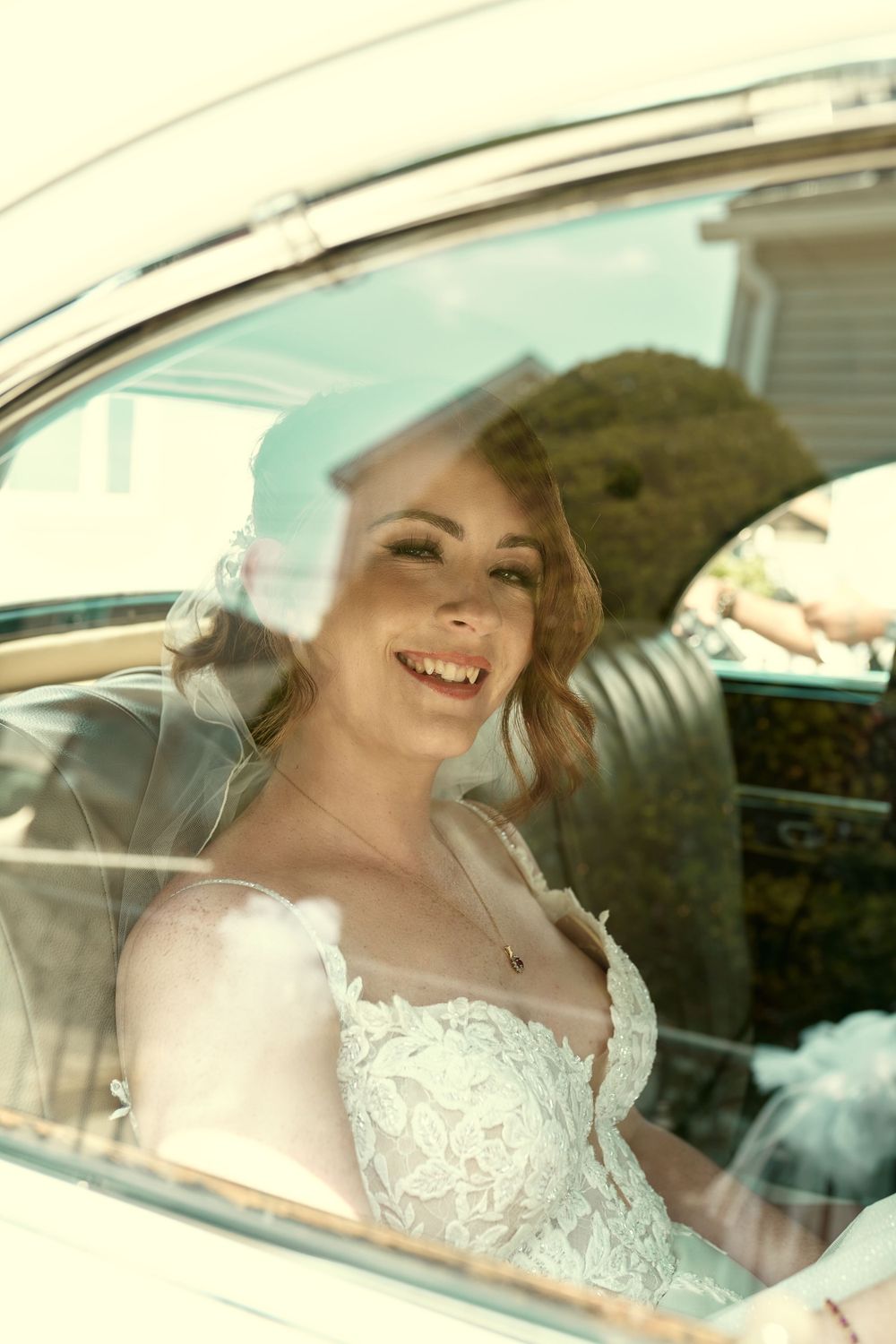 A radiant view of a bride in a lace wedding dress through a vintage car window.