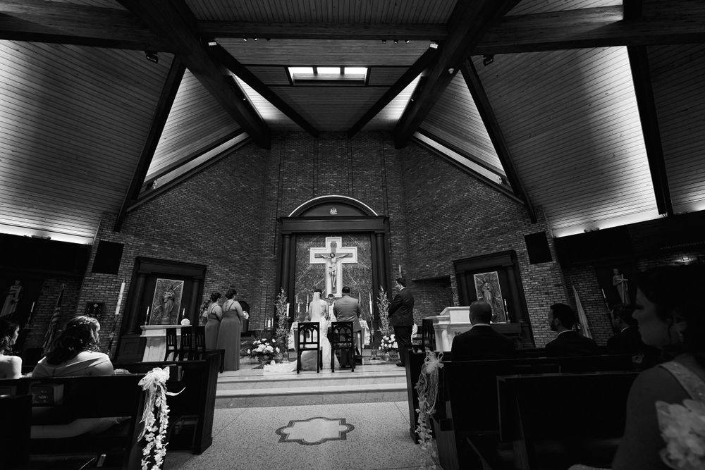 Black and white photo of a church wedding ceremony with dramatic lighting and cross at the altar.