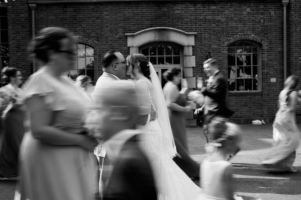 Black and white candid shot of wedding guests dancing and celebrating outside a brick building.