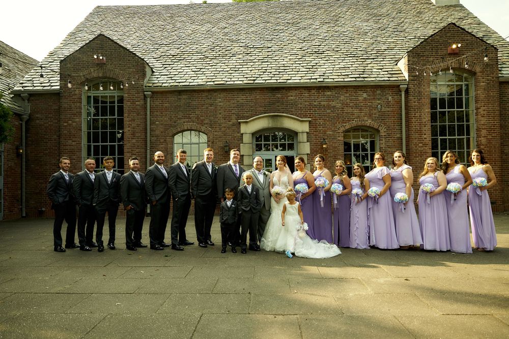 Wedding party poses in formal attire outside a classic brick church with purple bridesmaid dresses.