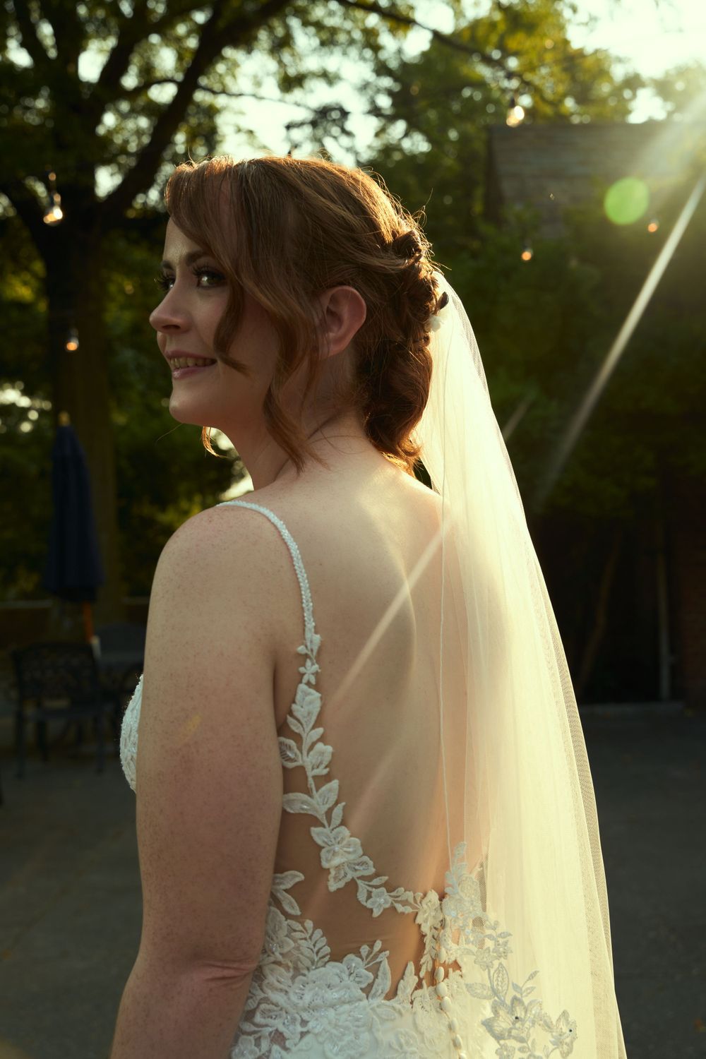Sunset portrait of a bride in a detailed lace gown with flowing veil against natural lighting.