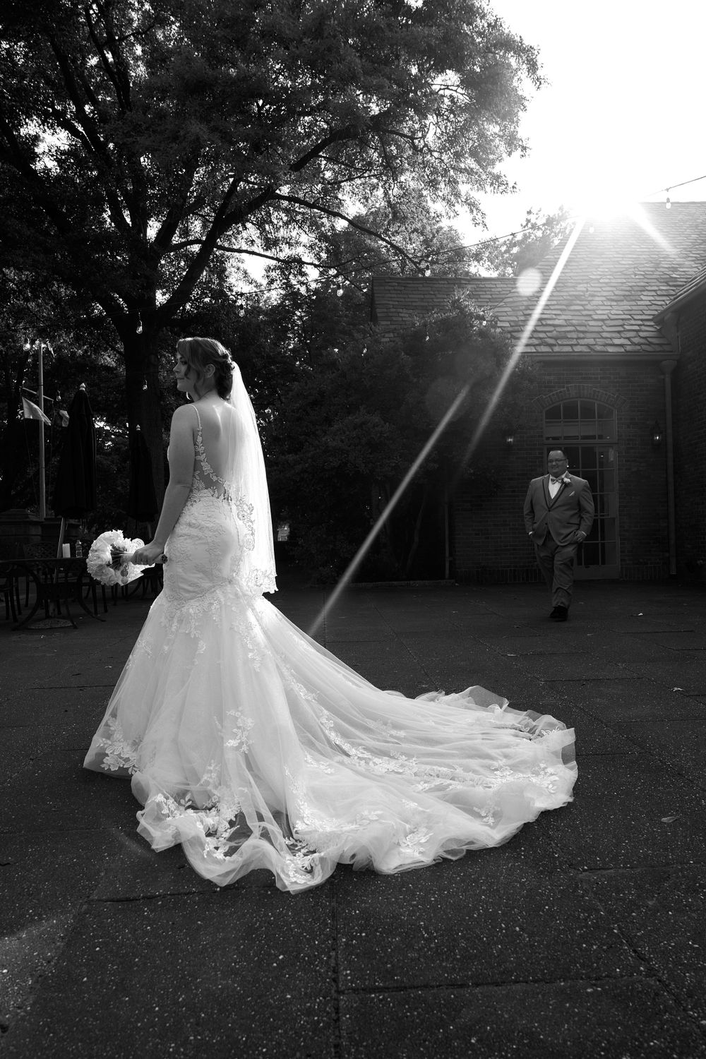 A flowing white wedding dress train spreads across a grassy lawn in dramatic black and white.