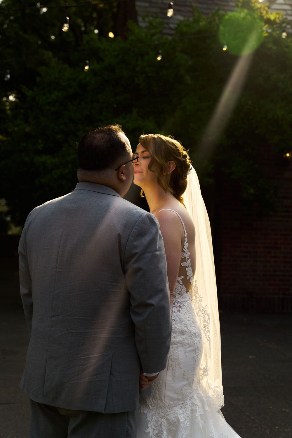 Romantic sunset wedding portrait with string lights and soft backlighting creating a dreamy atmosphere.