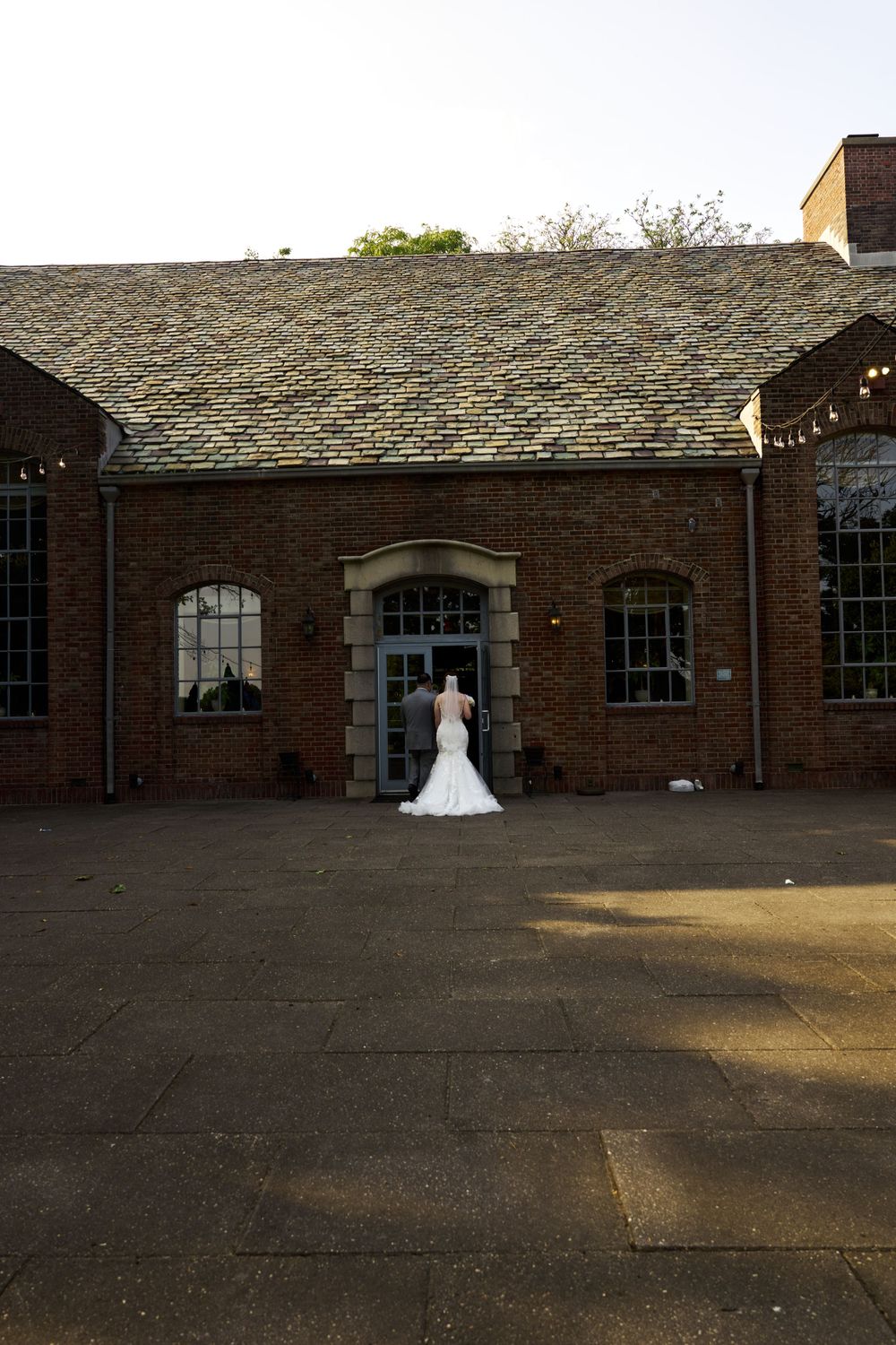 Long brick building with arched windows serves as backdrop for wedding photography at sunset.
