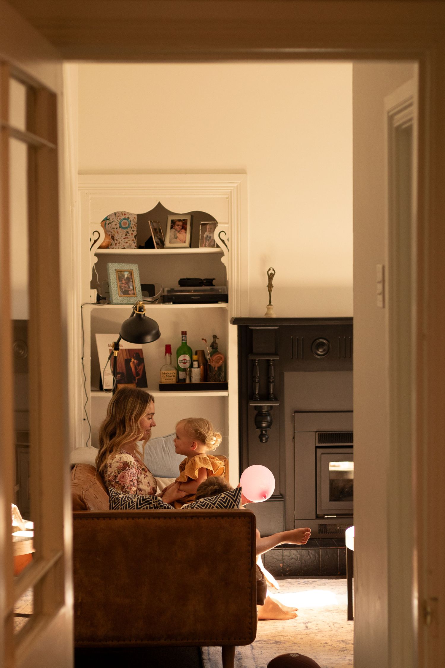 Two people relax on a brown couch in a dimly lit living room with warm lighting and minimalist decor.