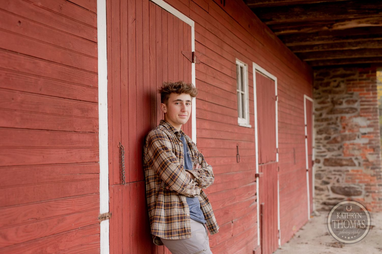 A casual portrait against a rustic red barn wall with someone wearing a plaid flannel shirt.