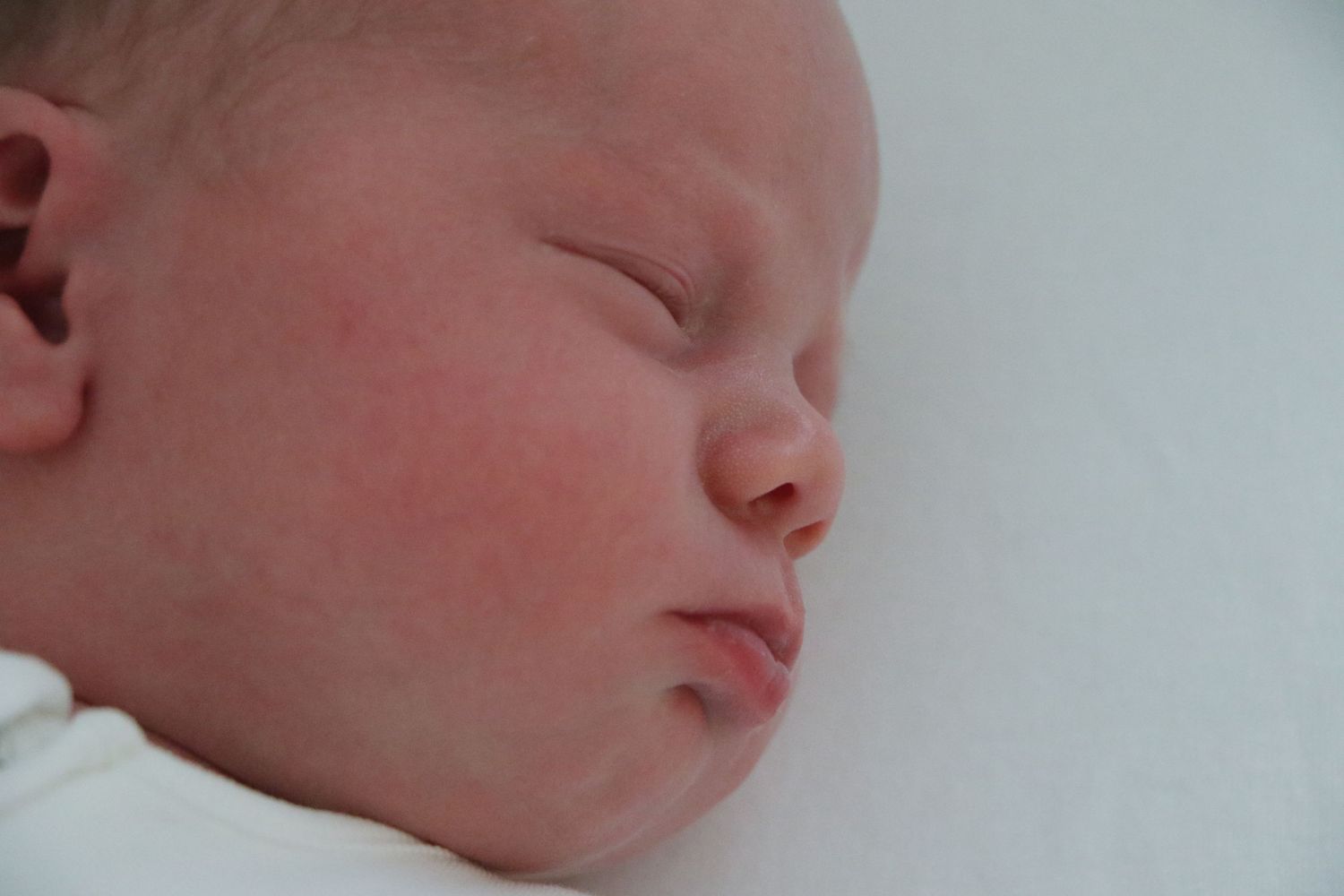A sleeping newborn baby's face with rosy cheeks against a soft white background.