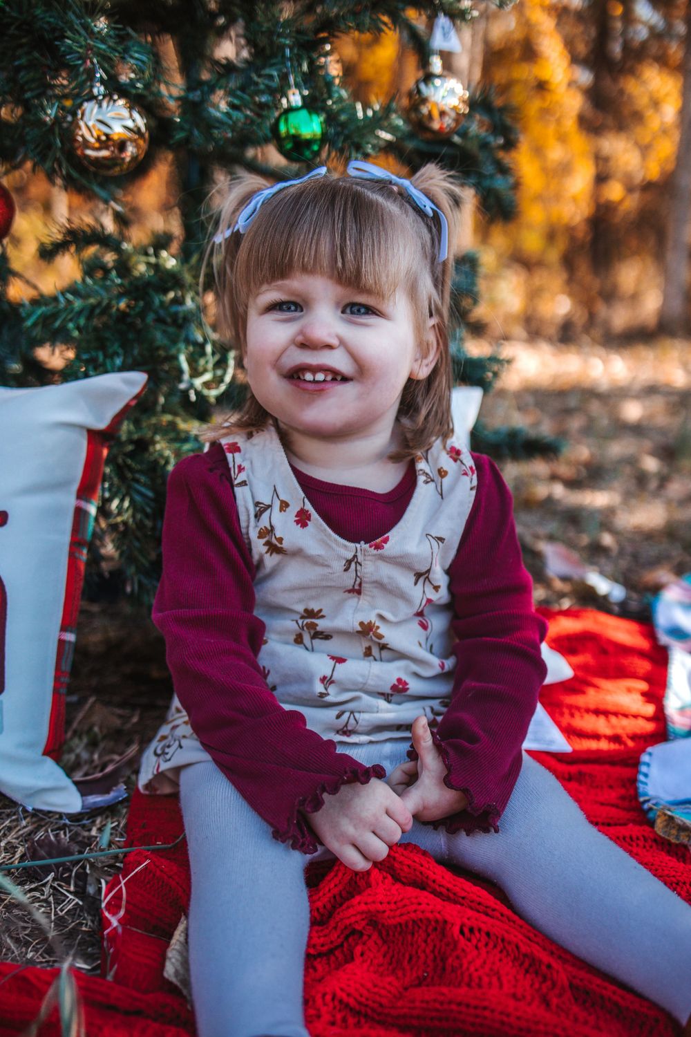 A festive holiday portrait of a child sitting by a Christmas tree with ornaments.