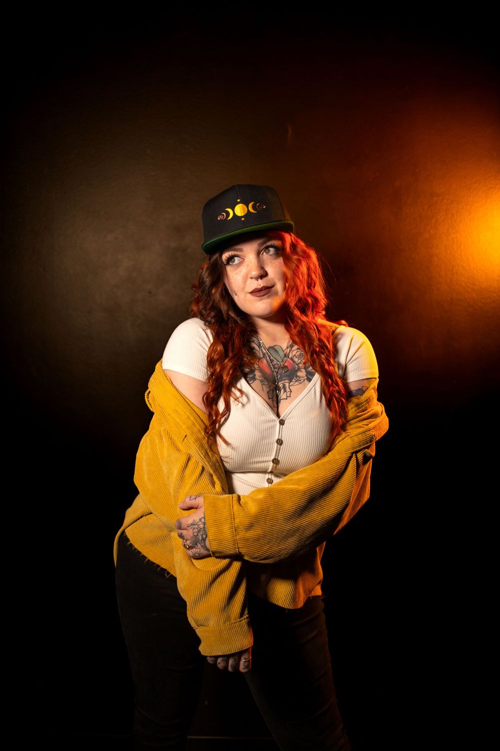 Studio portrait featuring a person in yellow jacket and cap against dark dramatic lighting.