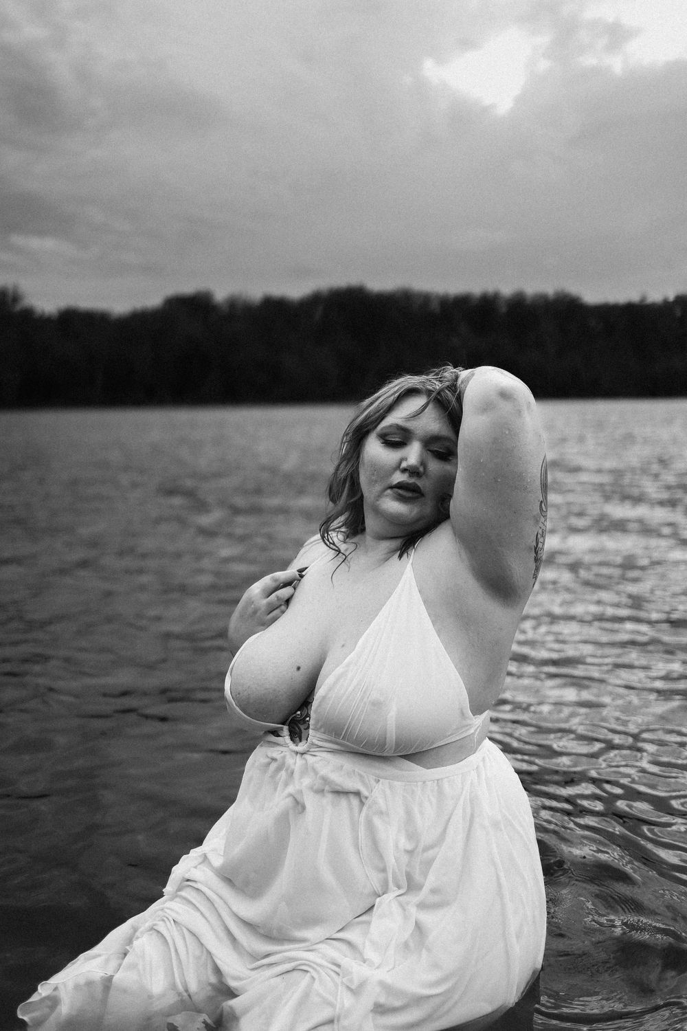 A moody black and white portrait of a woman in a white dress posing in water.