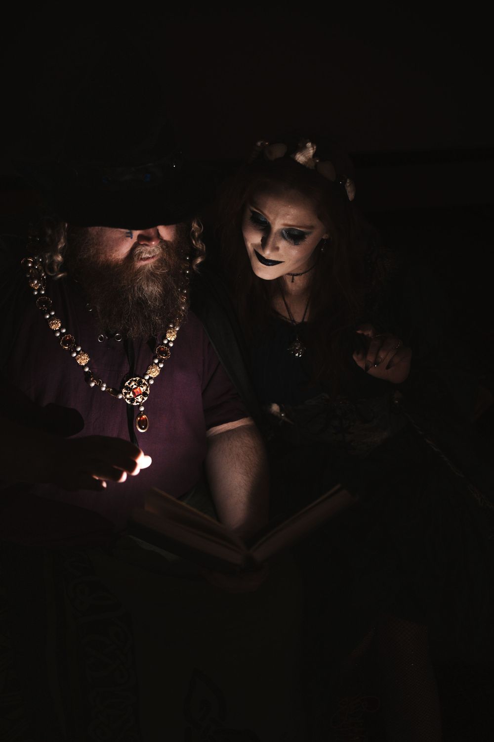 A darkly lit scene shows two people reading something illuminated by a dim light.