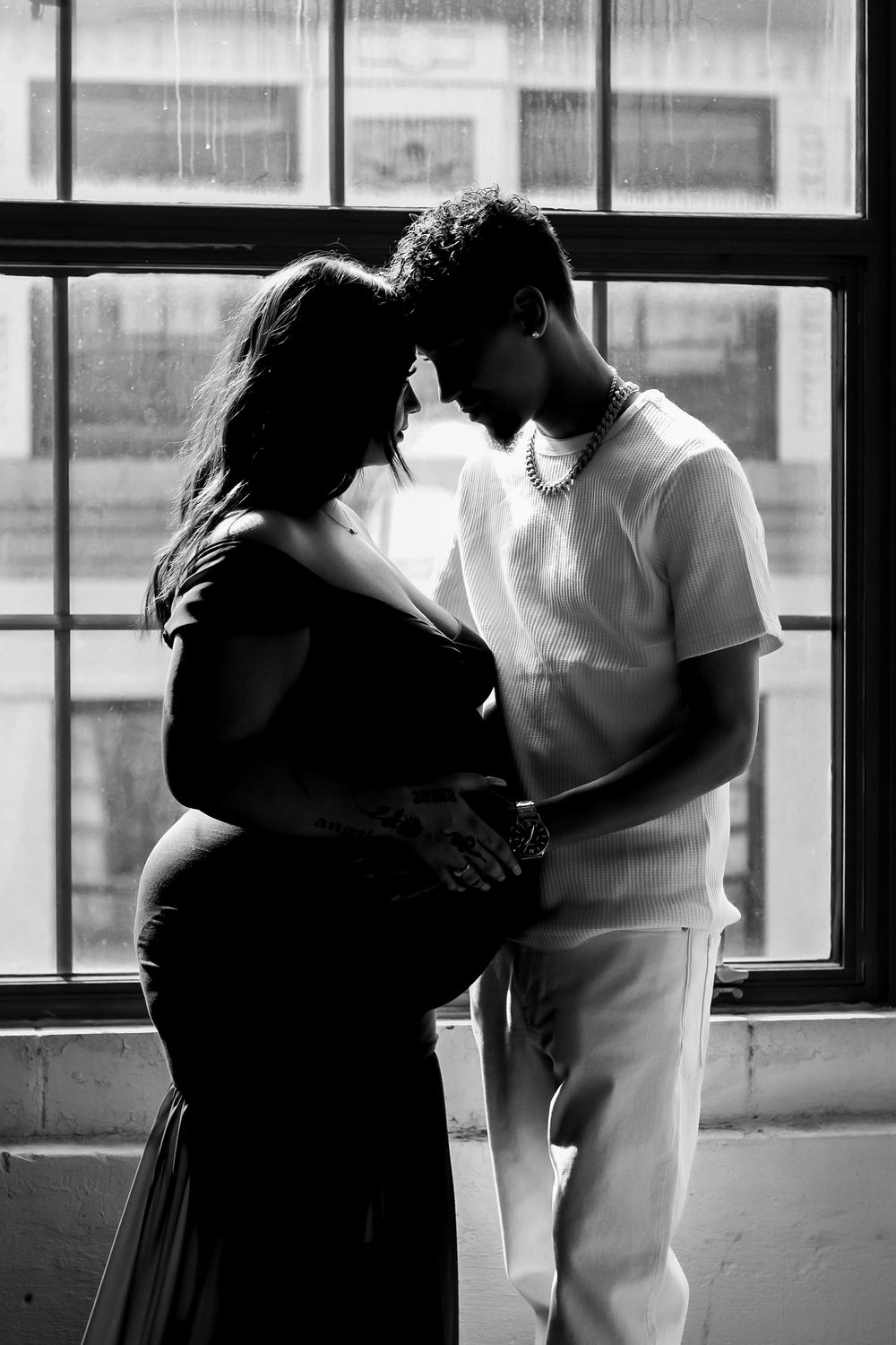 A silhouetted maternity photo showing a couple embracing near a window.