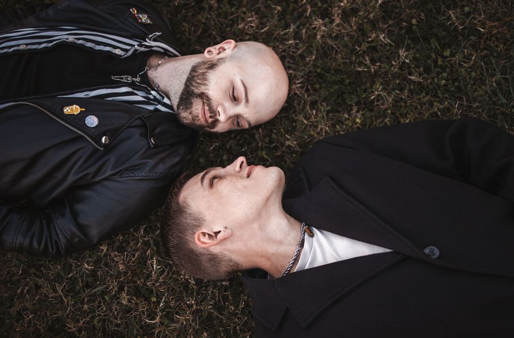 Two people lying on grass in dark clothing looking up at the sky.