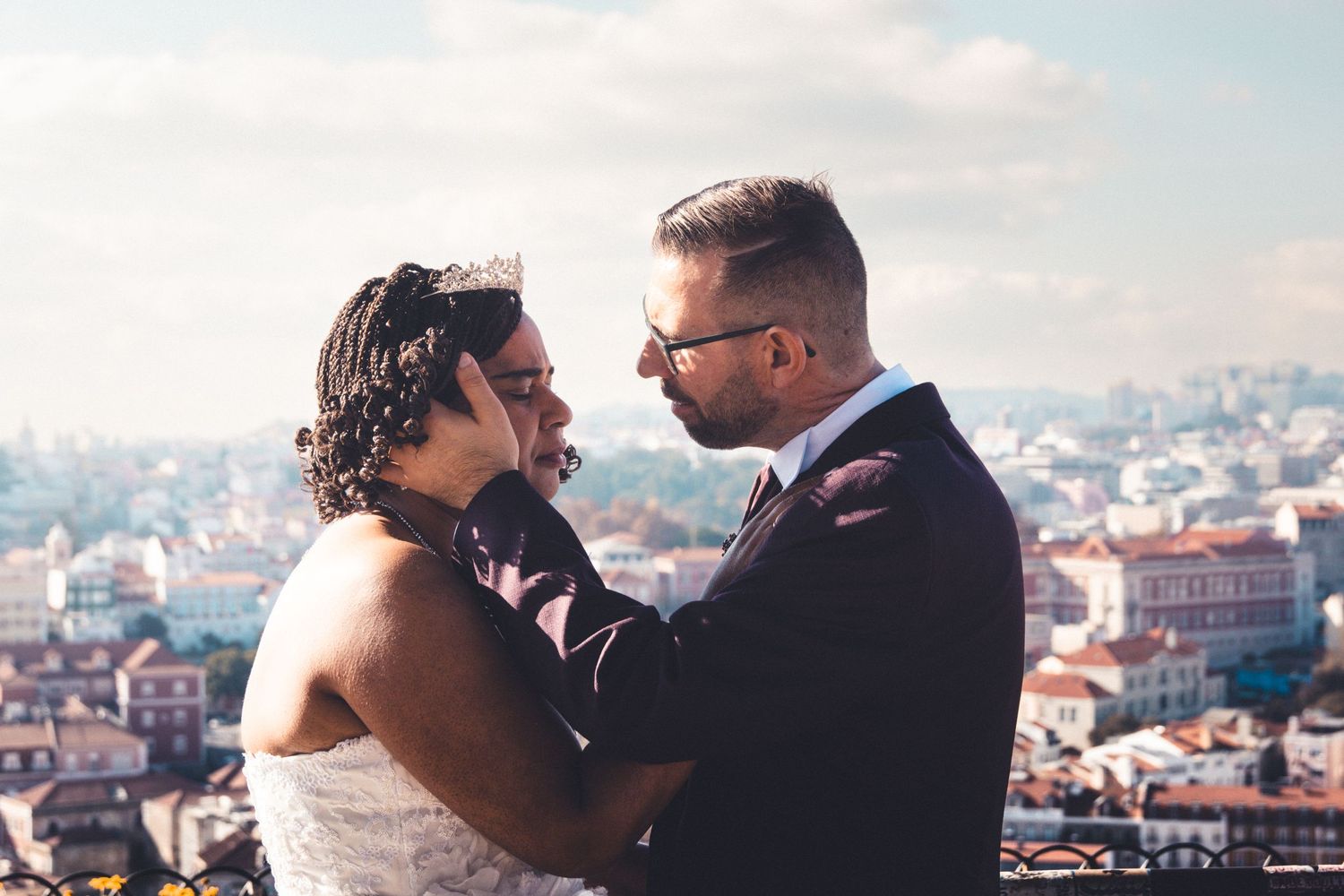 A romantic wedding couple embraces on a rooftop overlooking a European cityscape on their special day.