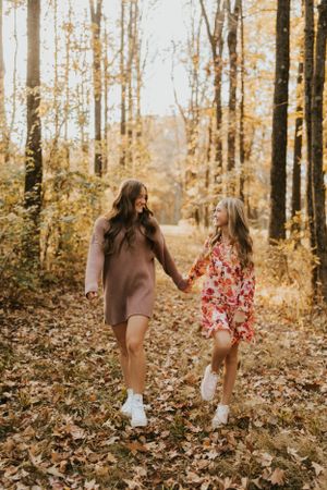 Two best friends wearing autumn dresses running through a forest looking happy.